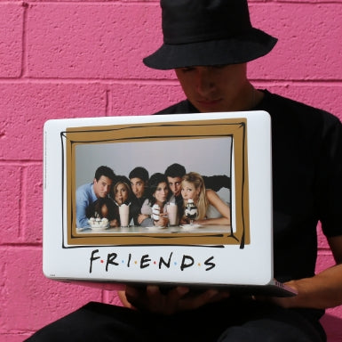 Man holding a laptop with a custom skin from the tv show Friends