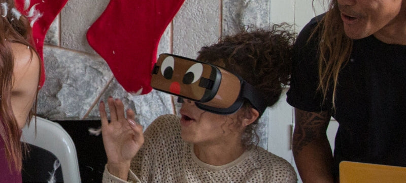 Person wearing a VR headset with a custom cartoon face skin while friends look on